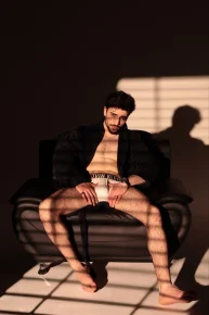 Masér Massimo v černém županu v křesle, stíny žaluzií